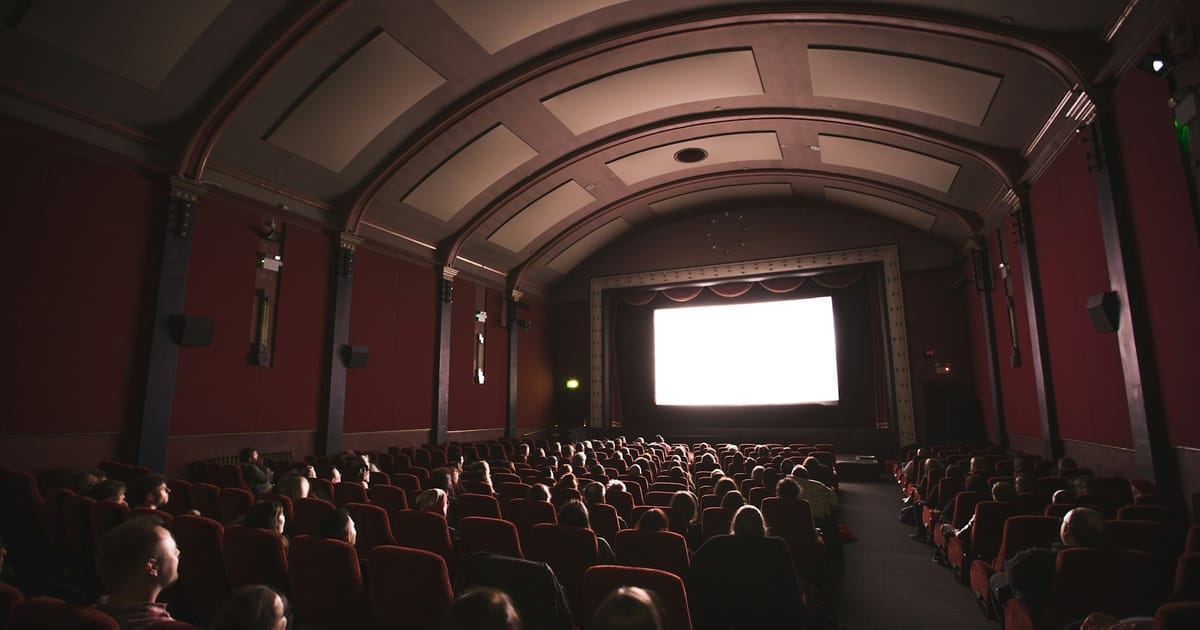 El público de una sala de cine a oscuras, con butacas rojas, mira una pantalla iluminada.