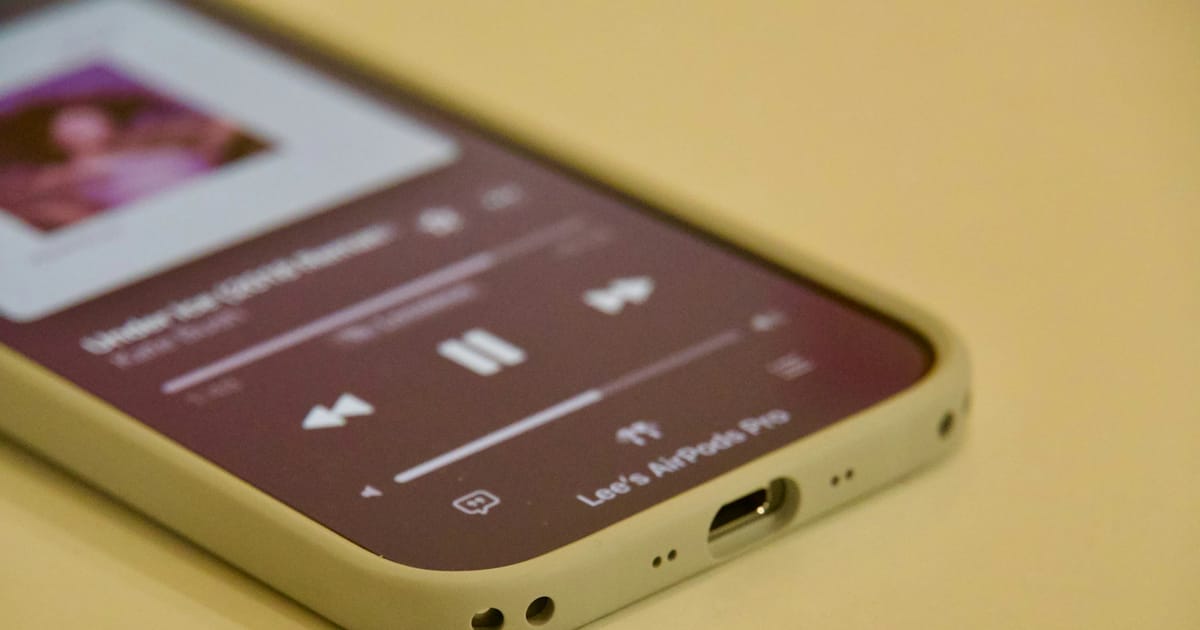 Un celular muestra la pantalla de una canción en reproducción sobre una superficie amarilla.