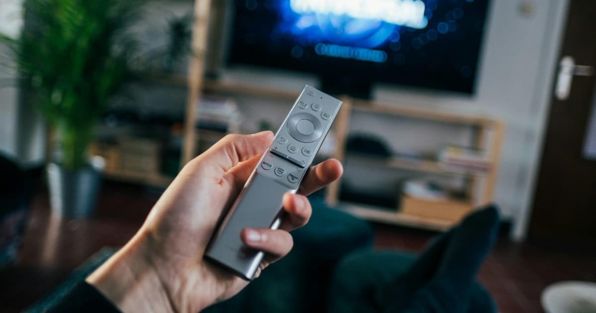 Un televisor sobre una repisa mientras una persona sostiene el control remoto.