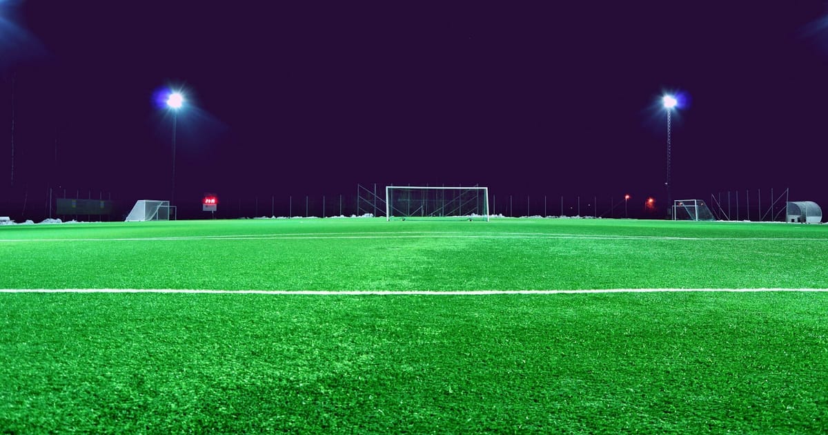 Una cancha de fútbol iluminada por las luces del estadio durante la noche.