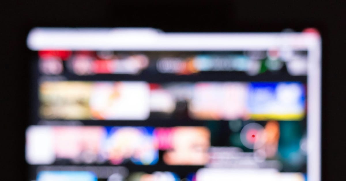 Un control remoto frente a un televisor que muestra una cuadrícula de contenidos desenfocada.