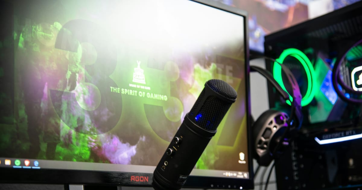 Un micrófono de escritorio frente a un monitor y una computadora con luces de colores.