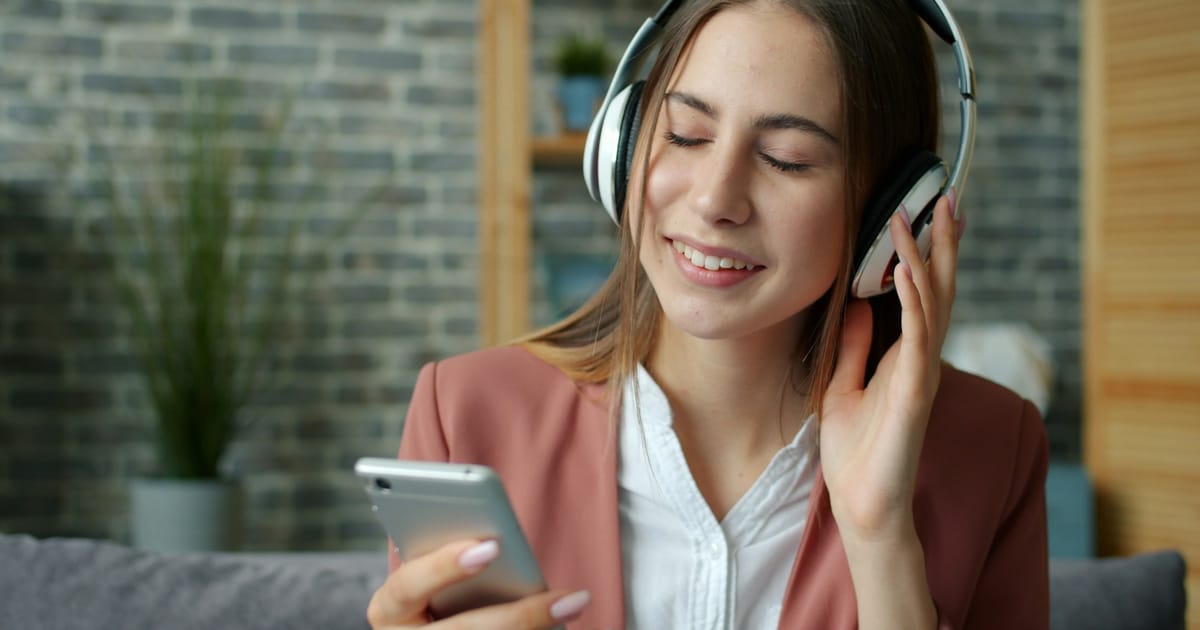Una persona escucha música con audífonos mientras mira su celular.