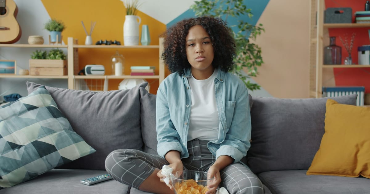 Una joven mira la televisión desde el sofá con un bol de snacks.
