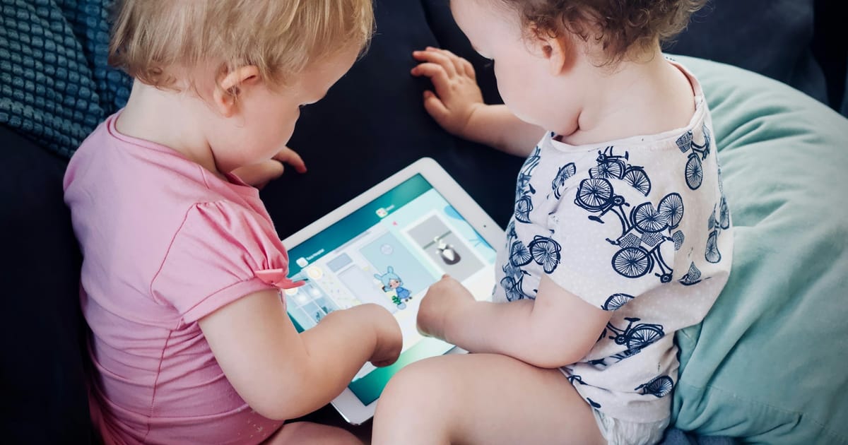 Dos niños pequeños miran juntos el contenido de una tablet en el sofá.